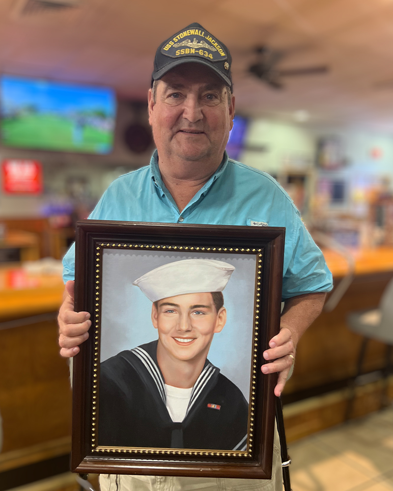 Man in Navy cap holding custom oil portrait of a young sailor